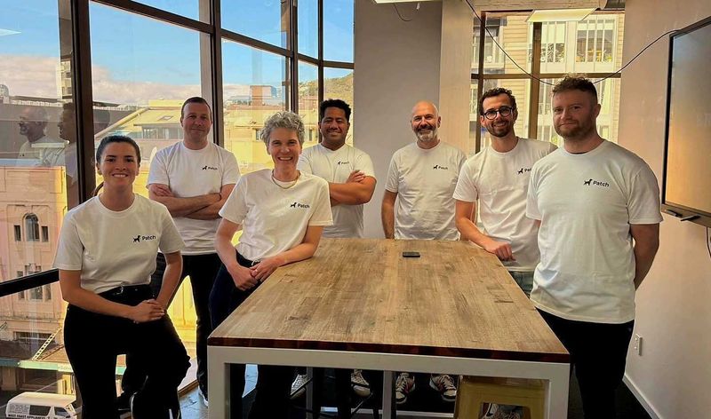 Some of the team gathered around a table in the Wellington office, with the city behind them.